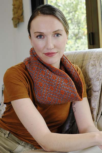 woman looking straight at camera wearing a mosaic knit cowl in colors charcoal/cinnamon.